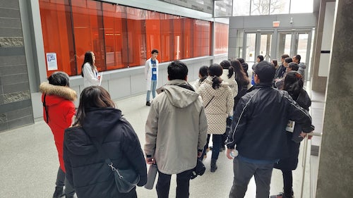 A student in a white lab coat conducts a tour of the Mike &amp; Ophelia Lazaridis Quantum-Nano Centre.