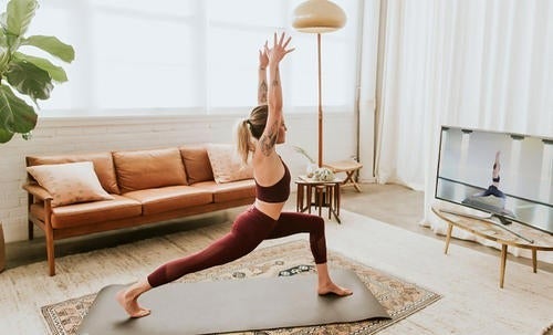 A woman does yoga in front of a television.