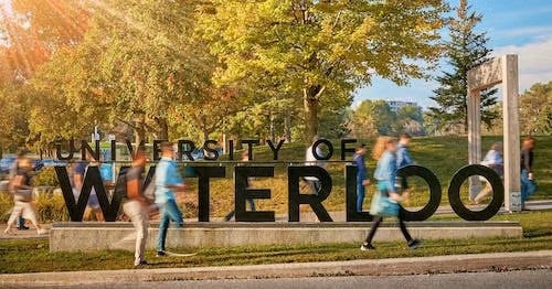 Blurred images of people walking past the University of Waterloo sign at its former location on University Avenue.