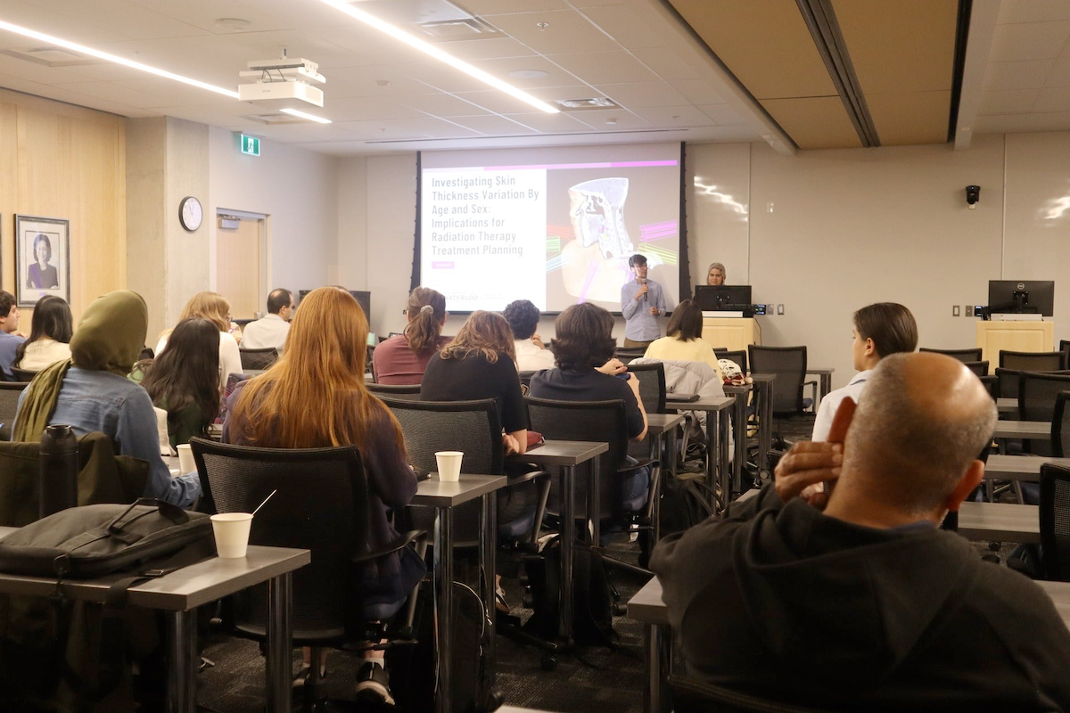 A person delivers a biomedical research presentation to a class full of students.