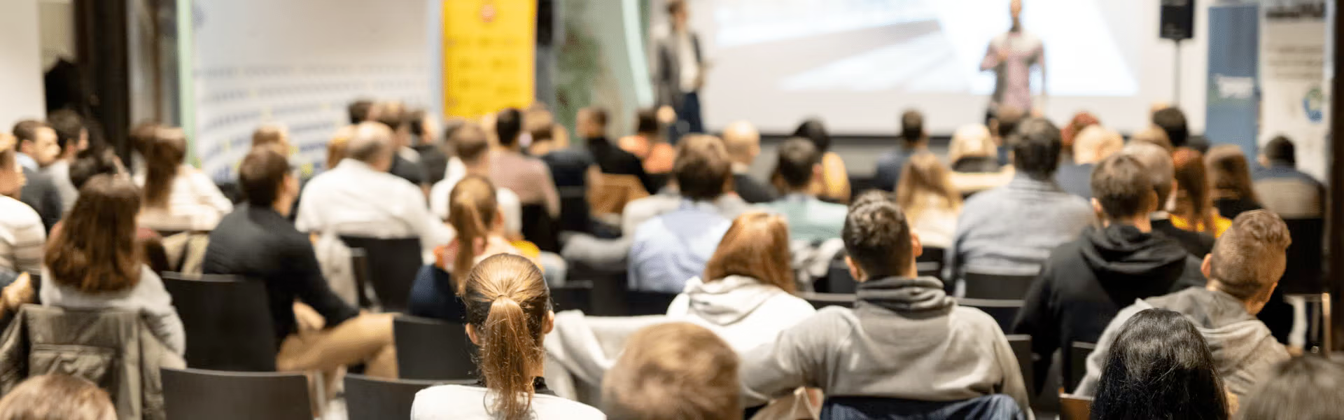 An audience watches presenters in a lecture hall.