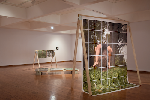 Art works hanging from a scaffold in a gallery.