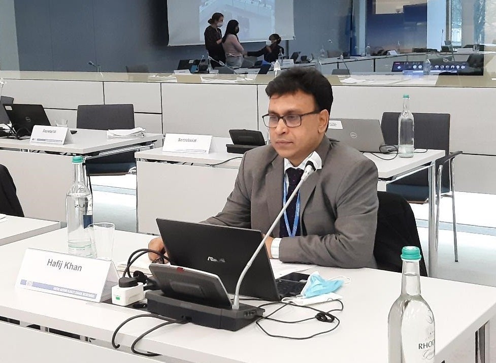 Hafij Khan seated at a table with a name placard, microphone and computer.