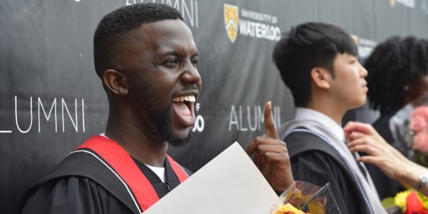 A smiling graduate gestures at Convocation.