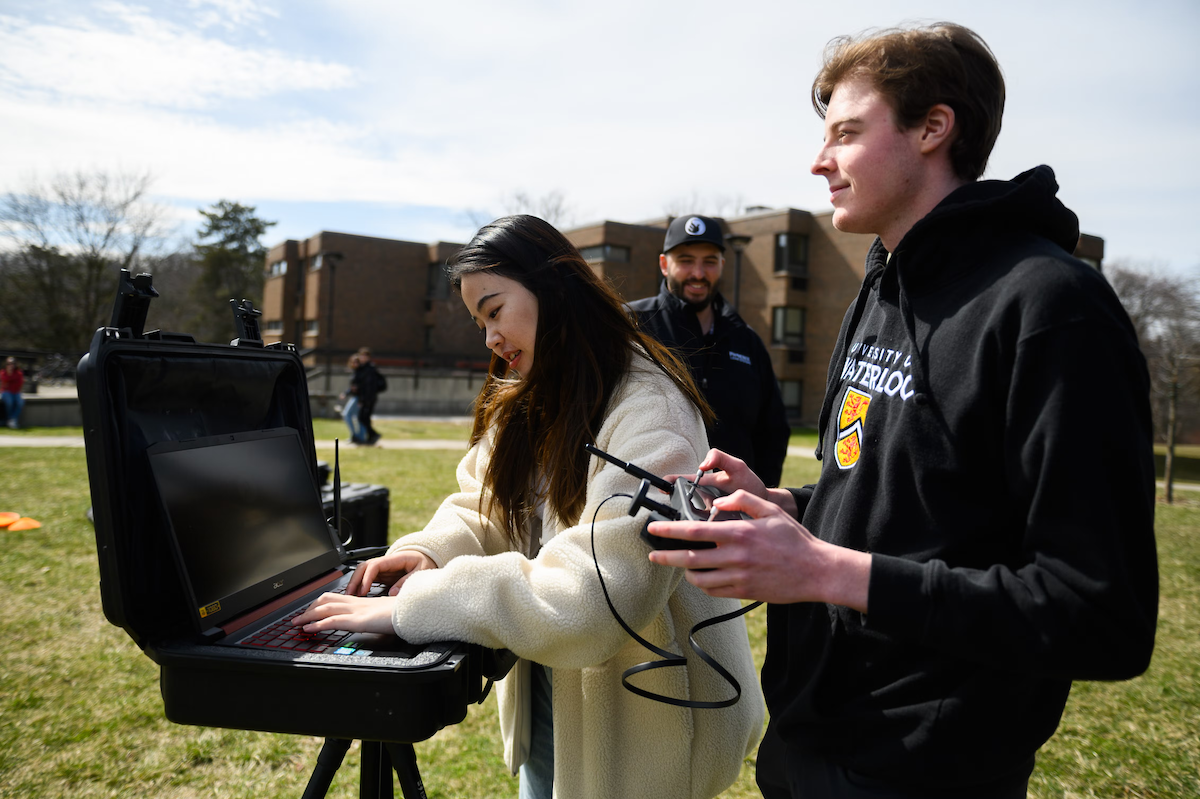 Students using a laptop on a stand to conduct geospatial research with the Minota Hagey residence in the background.
