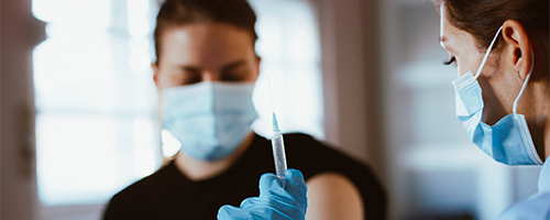 Two people in masks with a needle.