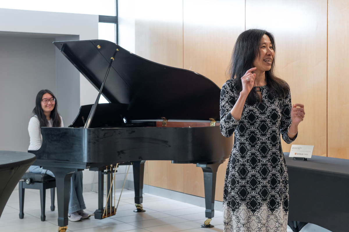 Professor Anita Layton speaks as a student sits behind a Boston baby grand piano.
