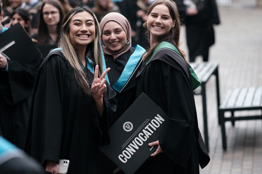 Three Waterloo graduands in regalia smiling with their diplomas.