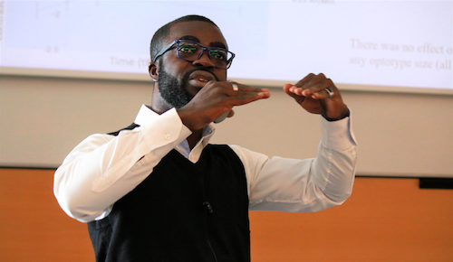 A man wearing glasses delivers a presentation.