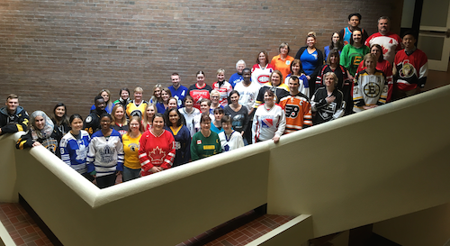 Members of the Registrar's Office wearing sports jerseys on the steps inside Needles Hall.