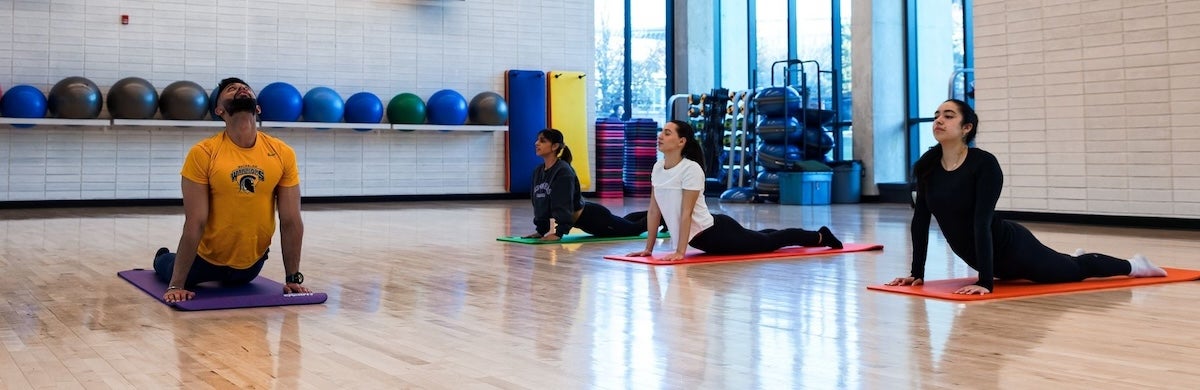 An instructor in a Waterloo Athletics shirt leads three women in a yoga class.