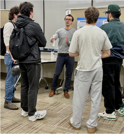 Brodric Uniac stands by his presentation board as onlookers look on.