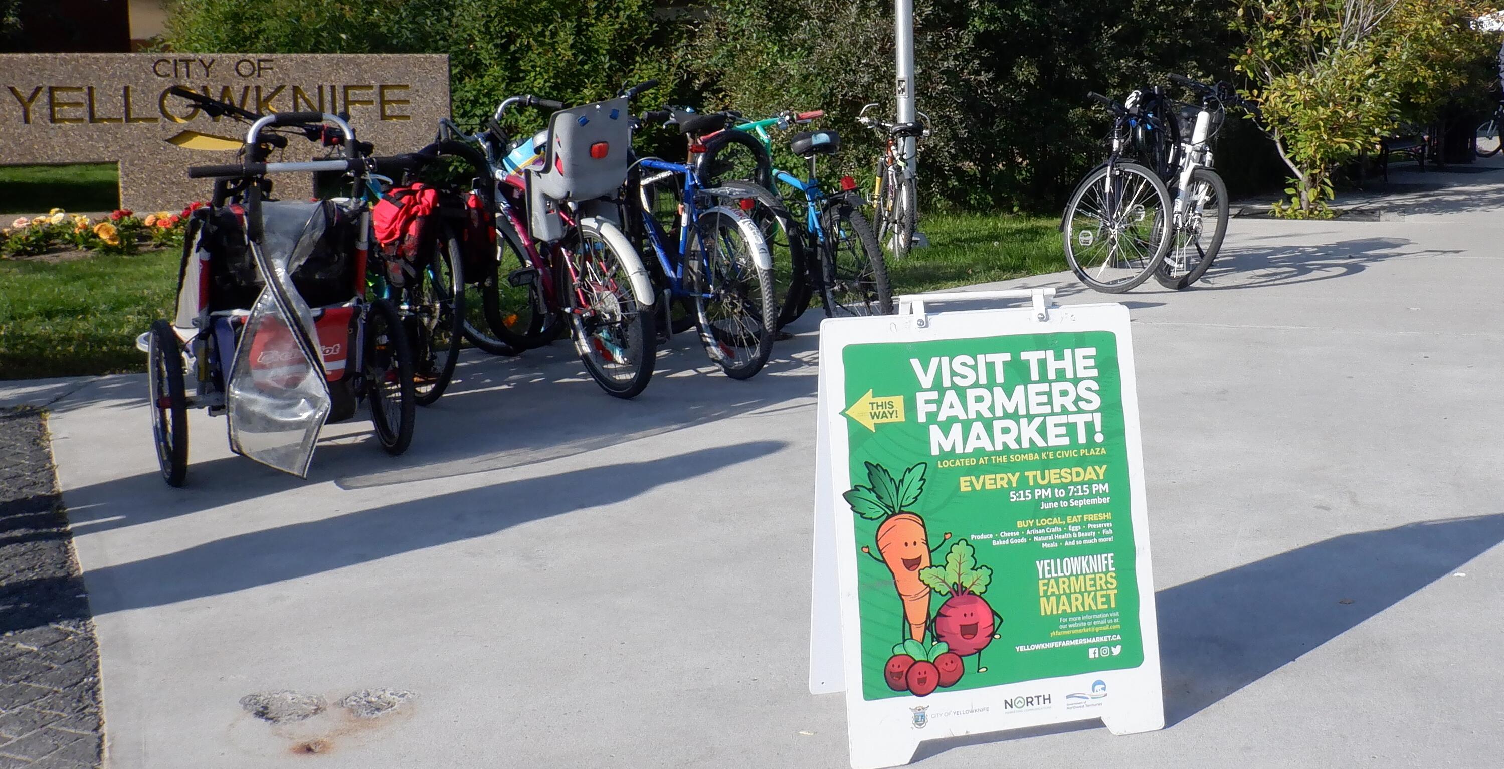 A sign for the Yellowknife Farmers Market in front of a rack full of bicycles.