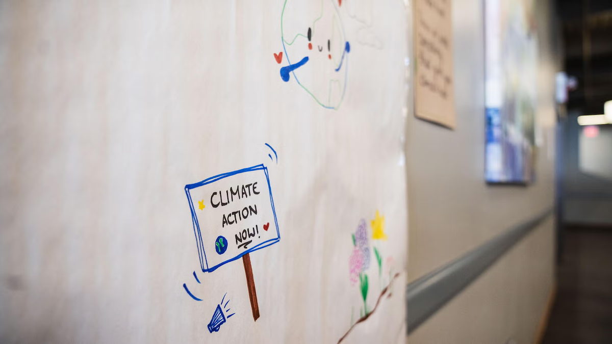 A hand-drawn poster on a wall with a sign that says "climate action now."
