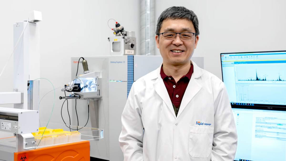 Dr. Bin Ma wears a white coat as he stands in his lab.