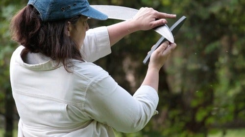A woman sharpens a scythe with a whetstone.