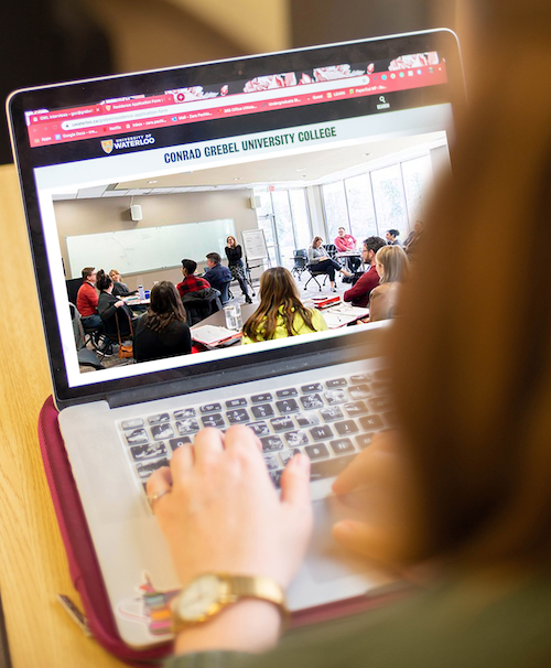 A laptop opened to the Conrad Grebel University College website.