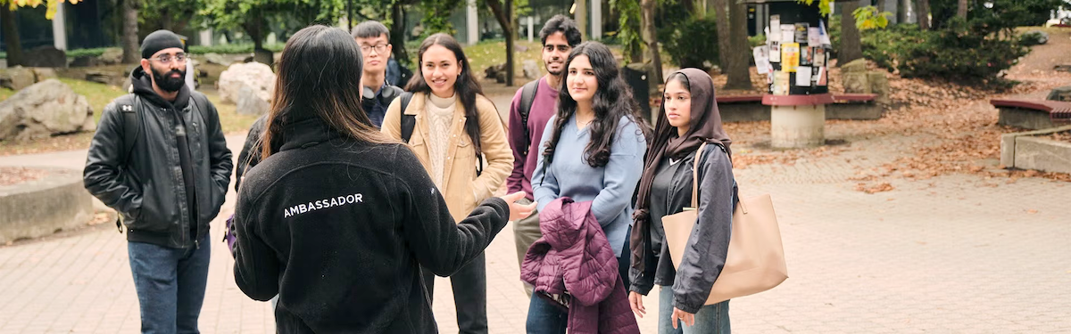 A person wearing an "ambassador" jacket conducts a campus tour with a group of future students.