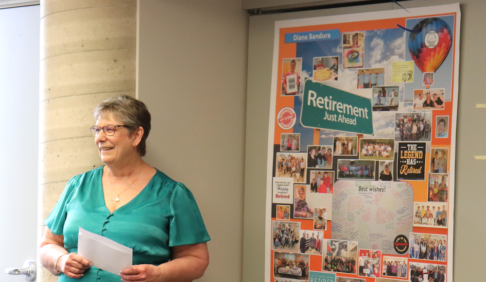 Diane Bandura stands next to a poster made for her retirement celebration.