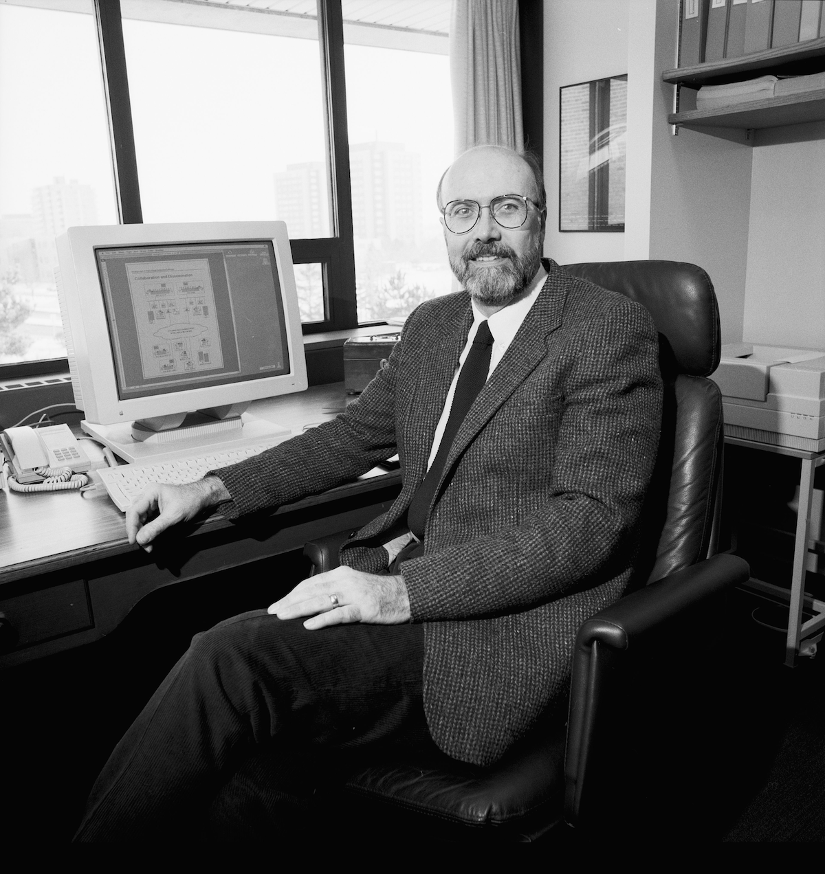 Dr. Paul Guild sits at a desk in his office with a PC monitor close by.
