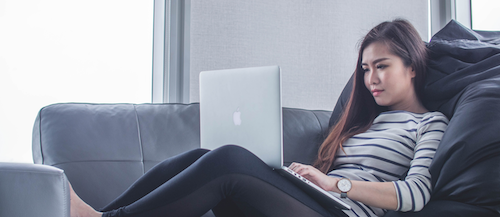 A woman sits on a couch while using a laptop.