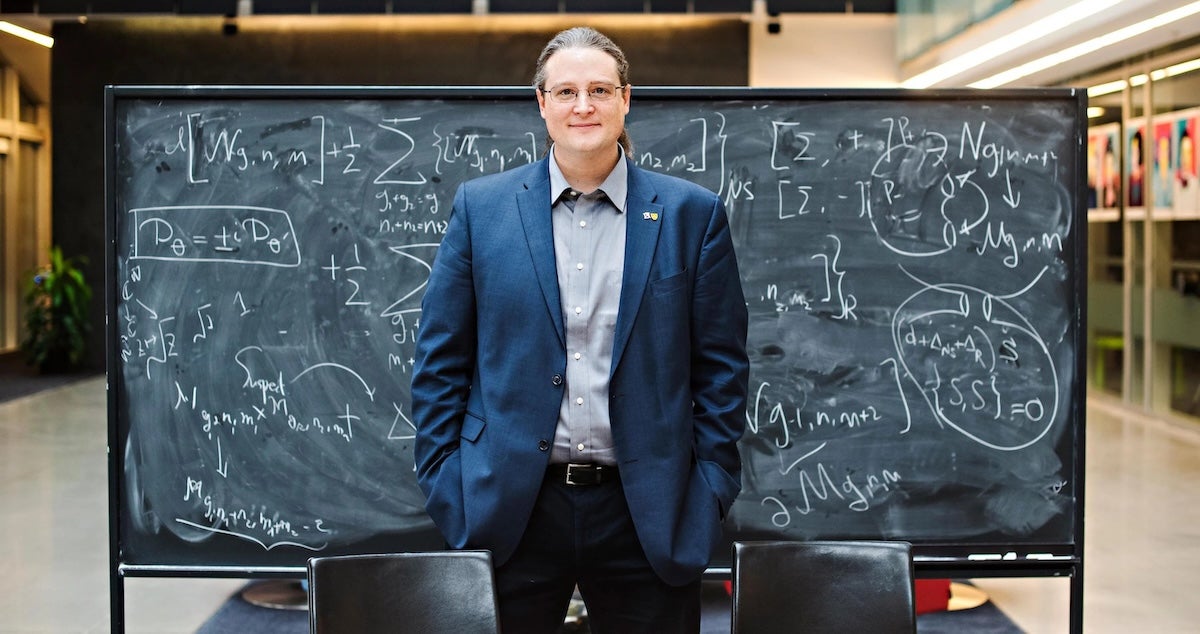 Dr. Avery Broderick stands in front of a blackboard full of math equations.