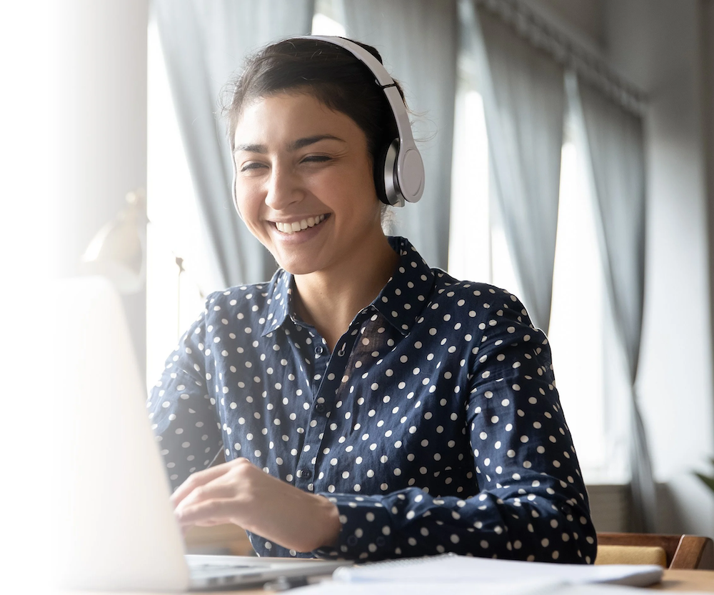 A woman wearing a headset smiles as she interacts with her laptop.