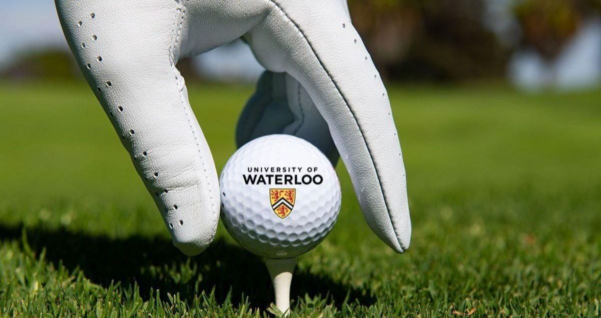 A person wearing a golf glove sets a University of Waterloo golf ball on a tee.