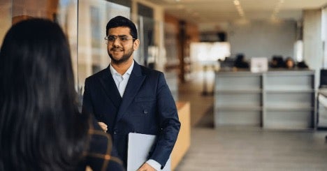 A man and a woman converse while standing in a hallway.