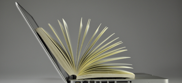 An open laptop with an open hardcover book on top of it.