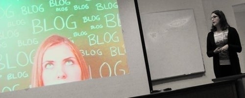 A woman stands in front of a PowerPoint presentation.