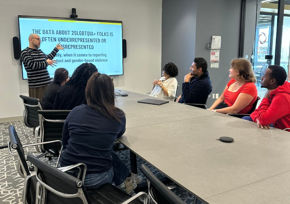 A man delivers a powerpoint presentation to a diverse group in the EDI-R board room.