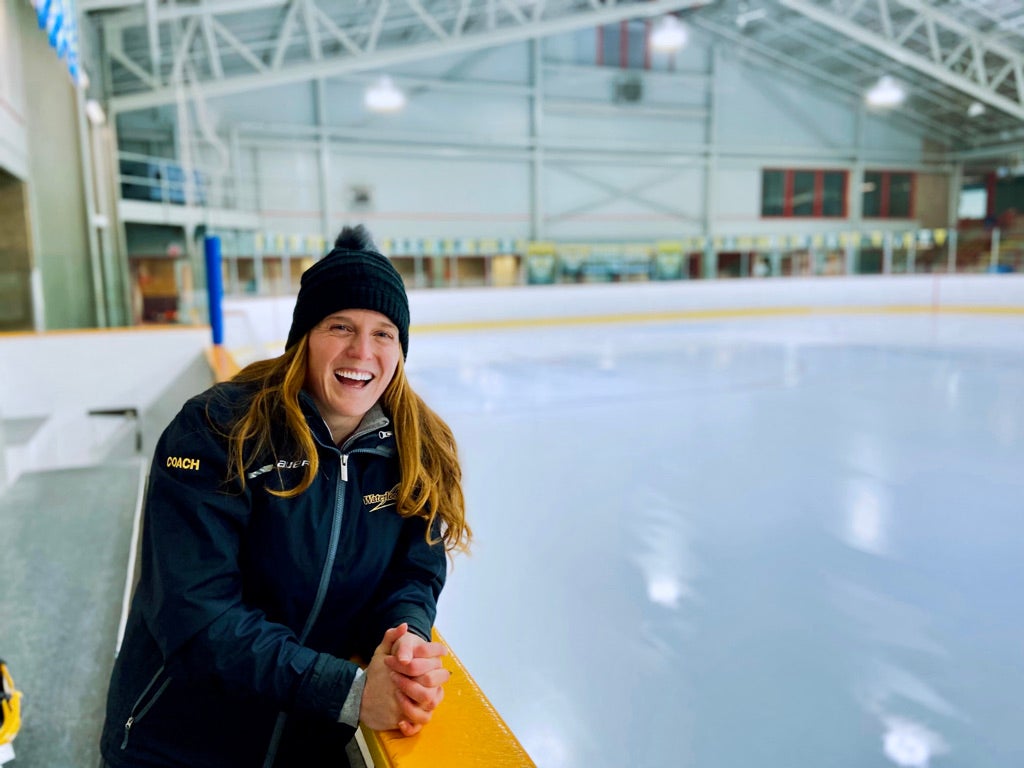 PhD candidate Haley Baxter stands next to an ice rink in an arena.
