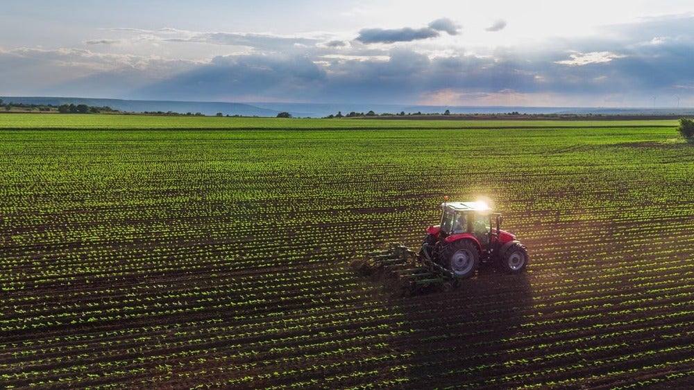 A tractor tends to the land in a wide open green field.