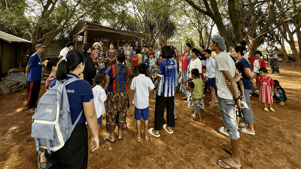 people gather round in a small village near a hut.