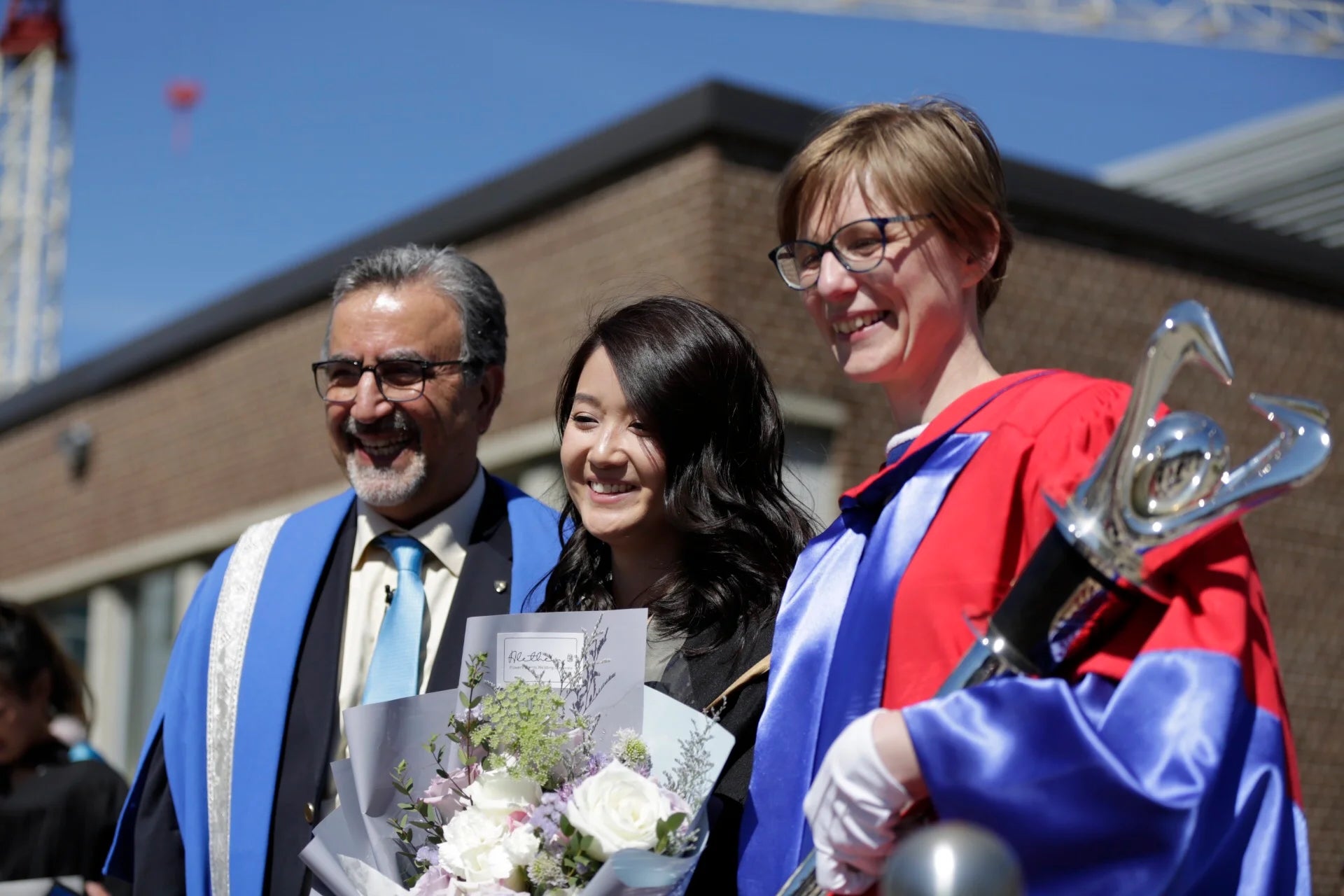 President Feridun Hamdullahpur, the mace bearer, and a student pose for a post-graduation photo.