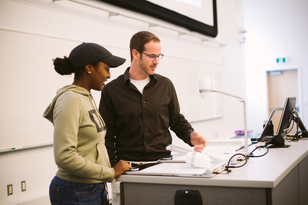 Faculty member talking to a student at a lecturn.