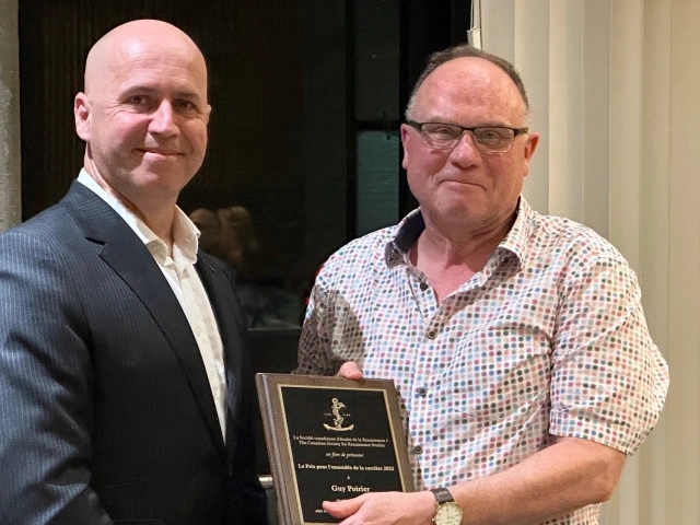 Dr. Guy Poirier receives a lifetime achievement award plaque from a representative of the Canadian Society for Renaissance Studies.