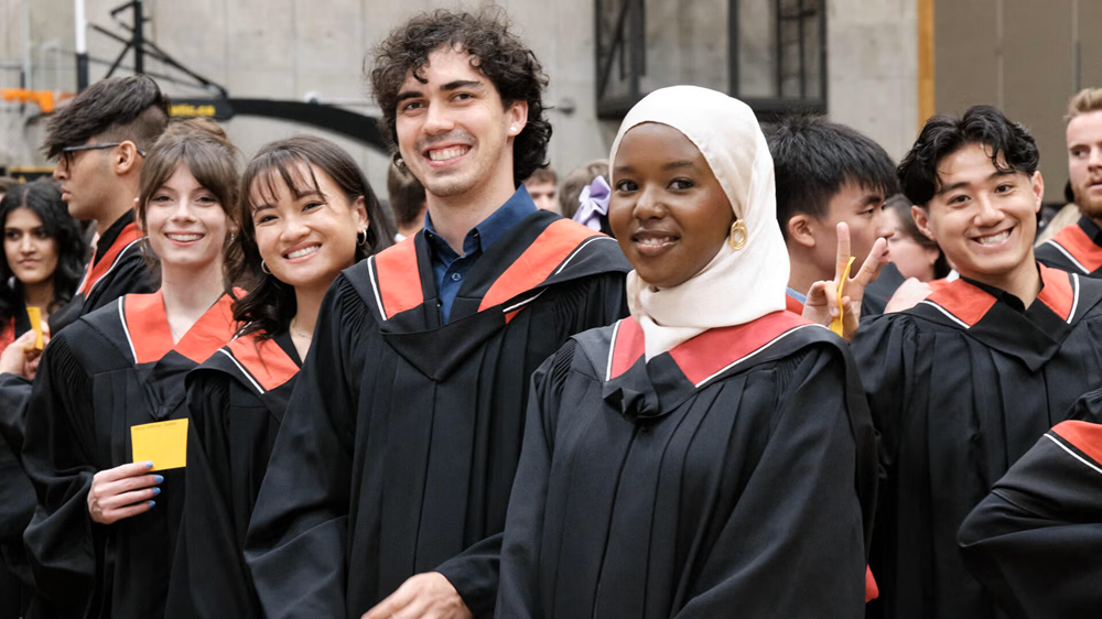 Students in full convocation regalia smiling.