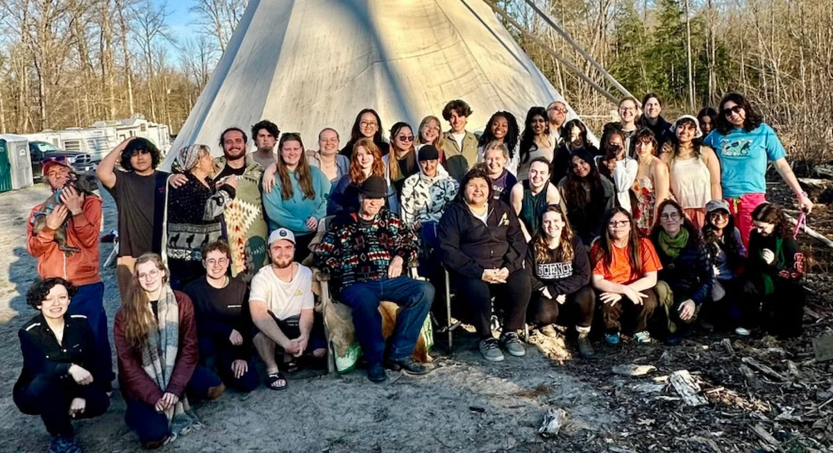 Students and Indigenous representatives in front of a traditional tipi.