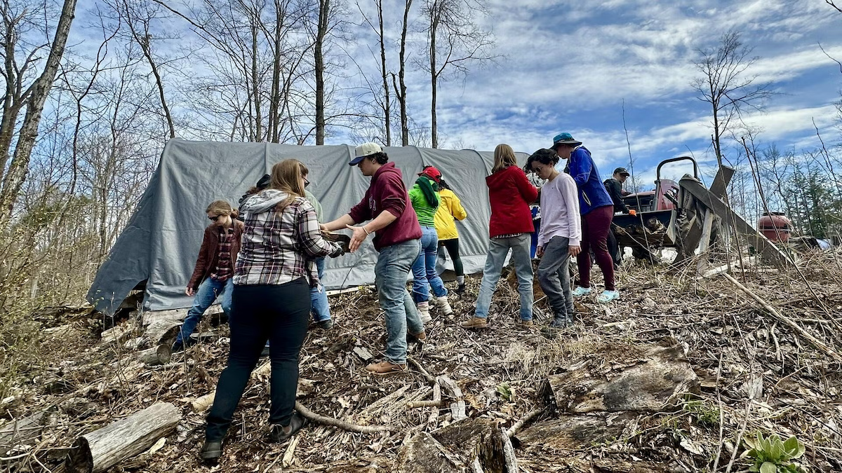 Students work in a field next to a covered shelter and a tractor.