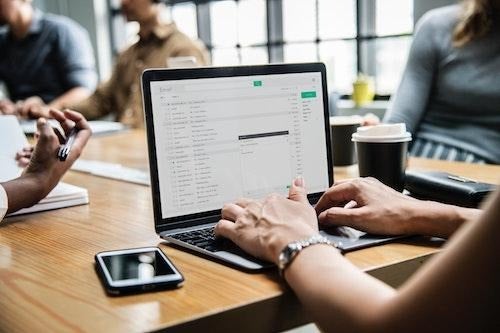 A person writes an email on a laptop at a conference table.