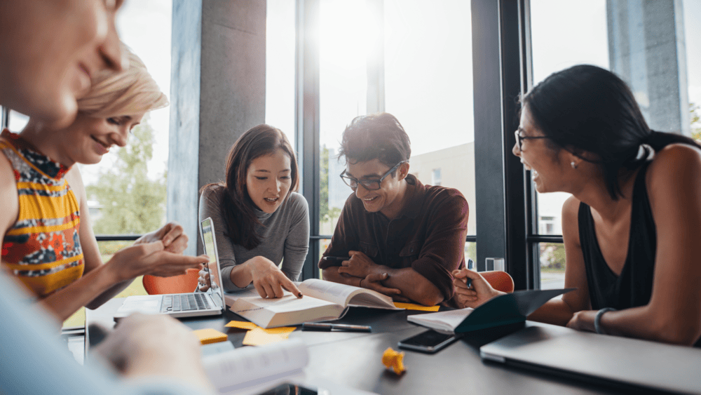 People sitting around a table looking at a book and phones.