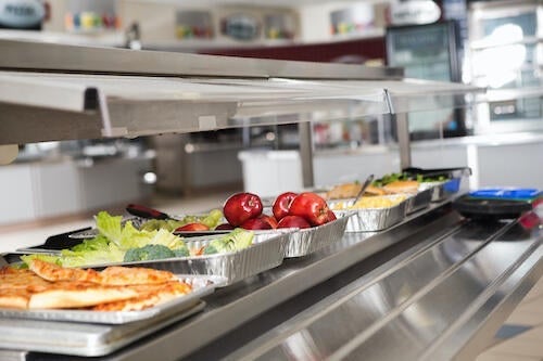 A cafeteria with a lineup of containers covered with foil.