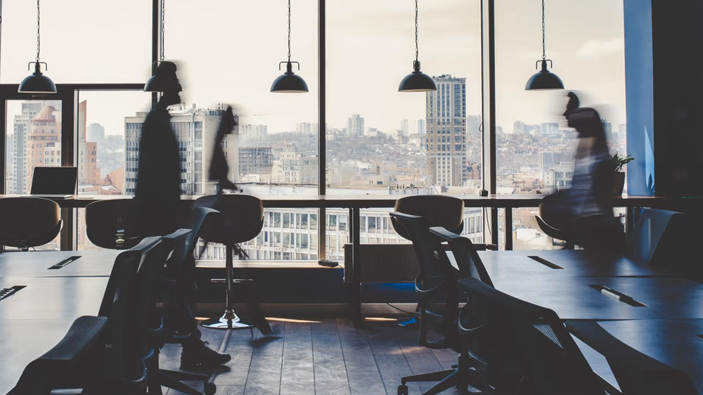 An out of focus view of a boardroom with people walking by a window.
