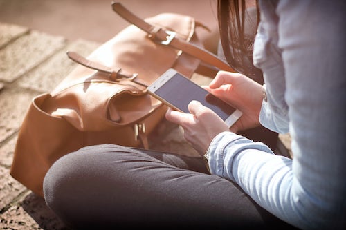 A woman uses a smartphone with a backpack in front of her.