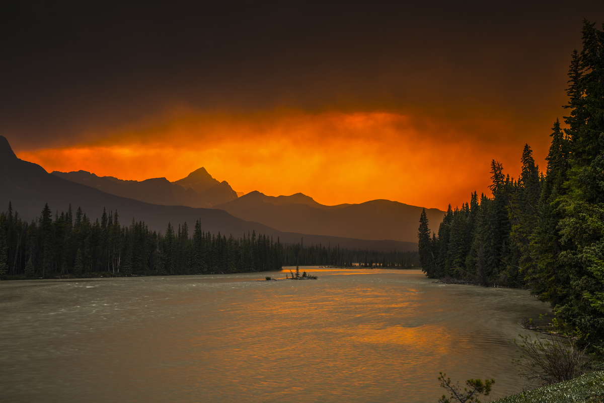 The mountains and lakes of Banff National Park backlit by the ominous orange glow of wildfire.