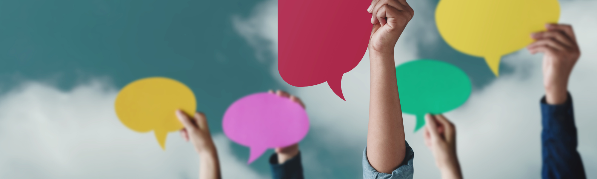 Five hands hold up different coloured speech bubbles against a blue cloudy sky.