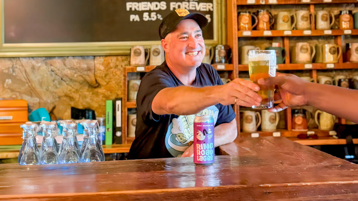 A smiling Jim Murphy stands behind a bar while handing a glass to a customer.