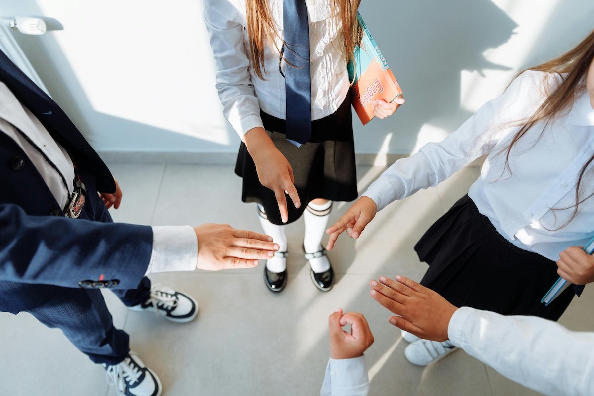 Children in school uniforms play a game of rock, paper, scissors.